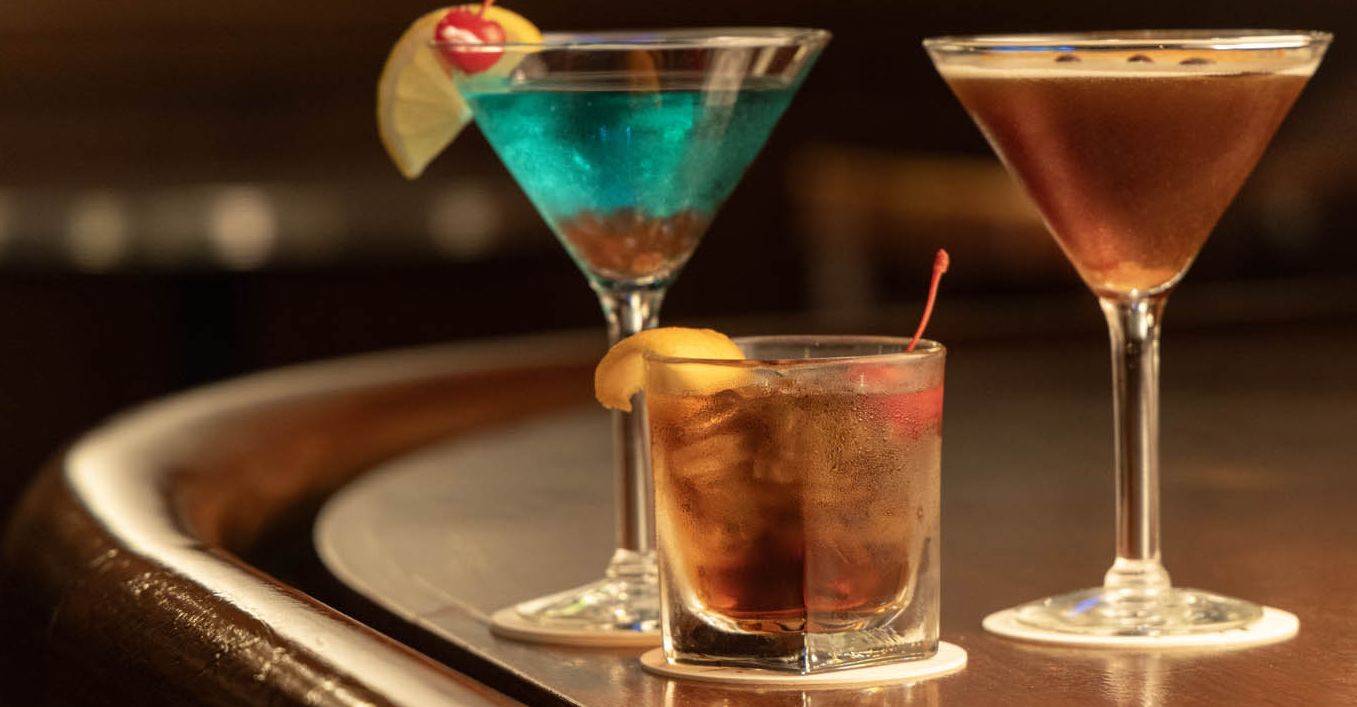 Colorful martinis and an Old Fashioned sit atop a mahogany bartop