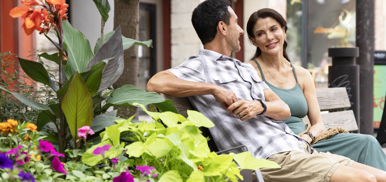 A couple sitting on a bench near some lush greenery on Ithaca Commons