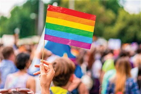 Hand holding a rainbow pride flag in foreground with a crowd in background